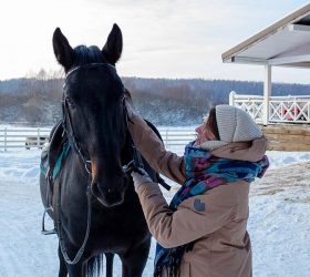 Frau in Winterbekleidung kümmert sich in den kalten Tagen um ihr Pferd