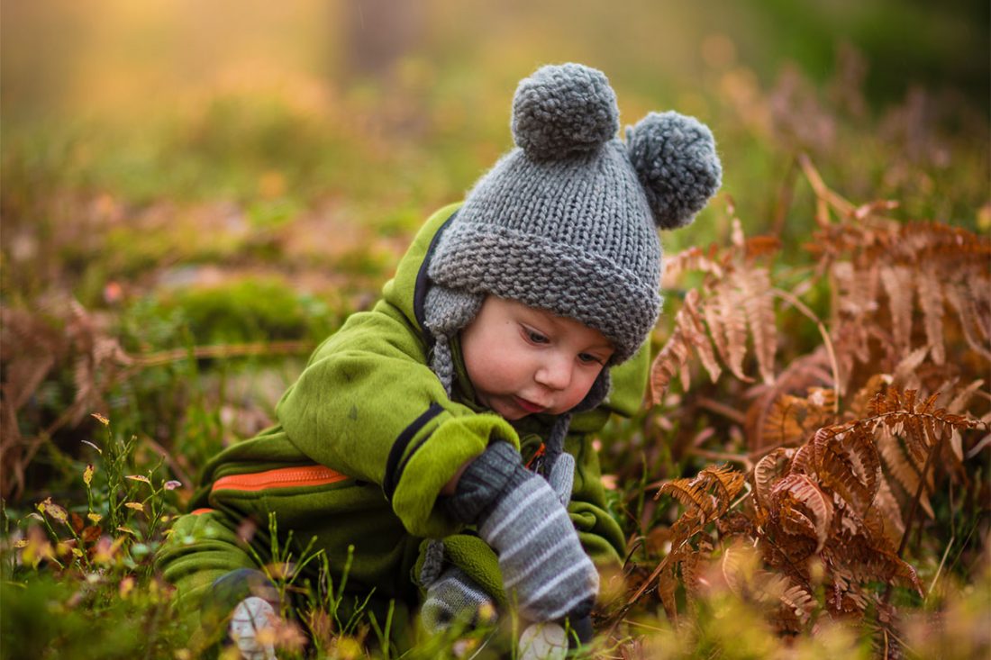 Kleiner Junge mit Bommelmütze spielt vergnüngt auf dem Waldboden